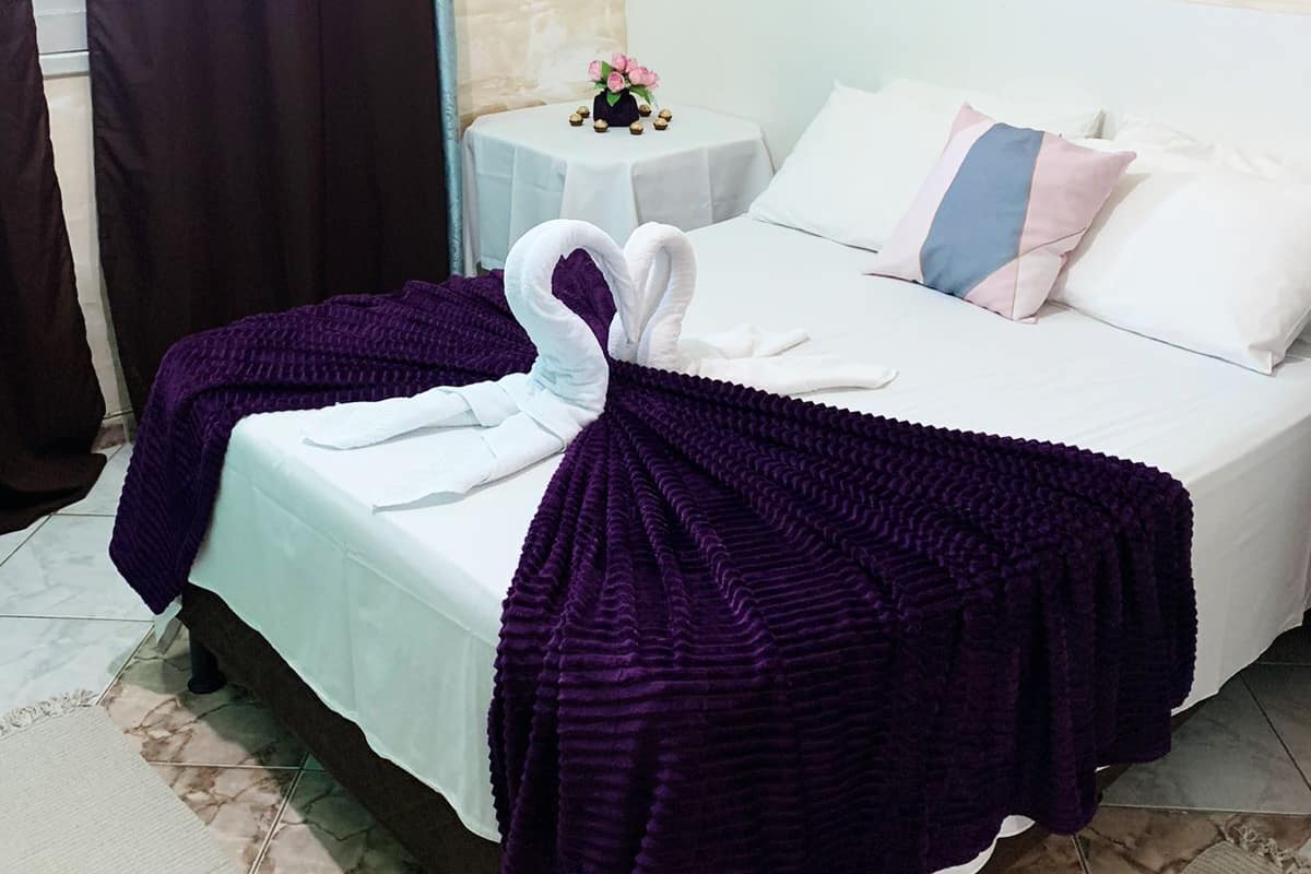 Habitación de hotel con cama, un cuadro en la pared, una mesita con un jarrón de flores y una cortina.