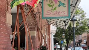 Un escaparate con un letrero que dice "Sisters Wine Bar" y una pizarra con el menú que ofrece cerveza y vino.