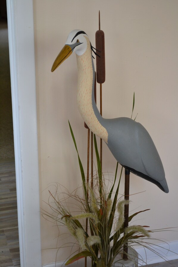 Una escultura decorativa de un pájaro con cuello largo y pico, junto a una planta de hojas verdes altas.