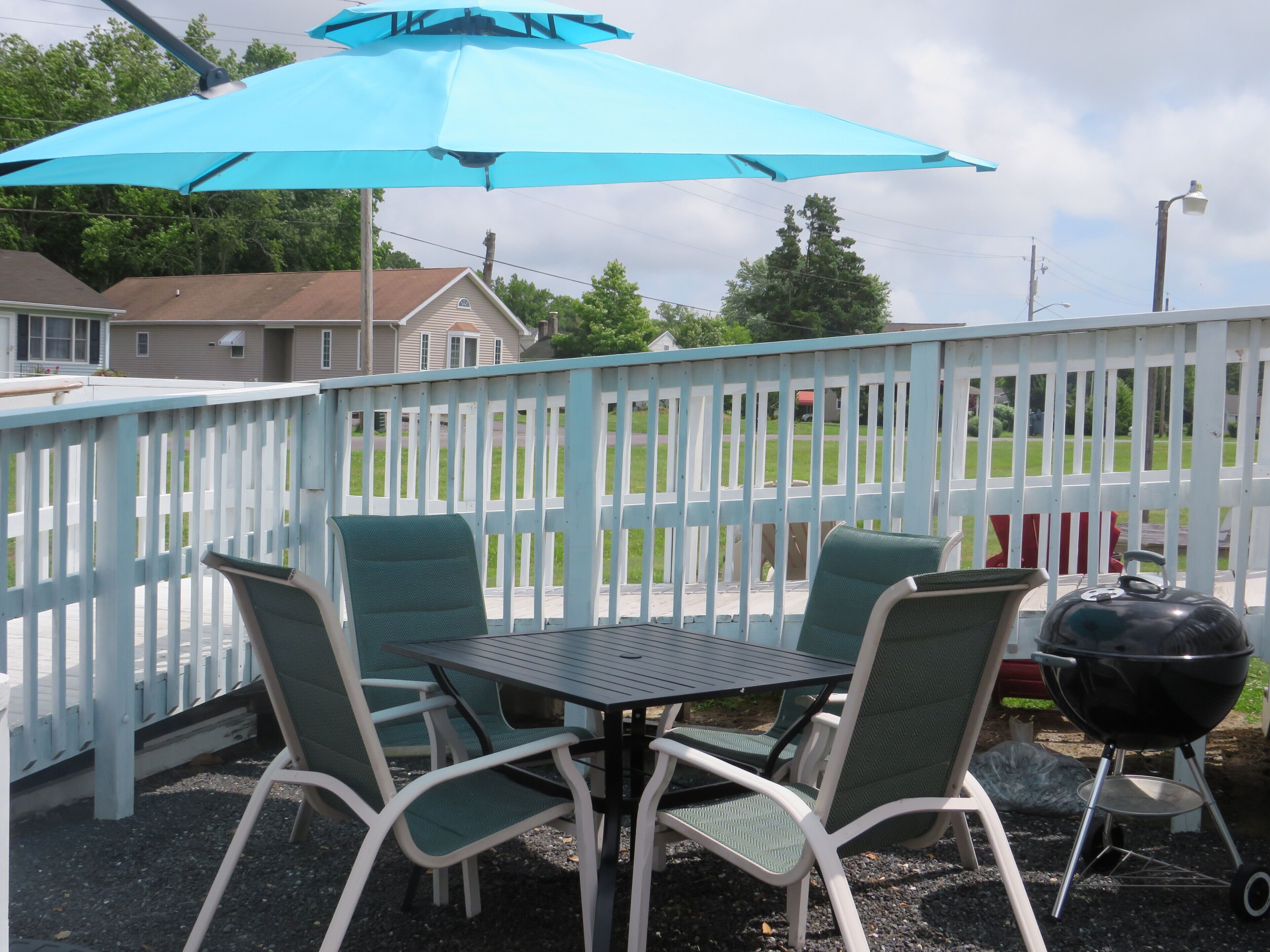 Eine Terrasse mit Tisch, Stühlen, einem Grill und einem blauen Sonnenschirm.
