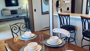 A dining area with a wooden table set for four, surrounded by chairs. A unique antler chandelier hangs above the table.
