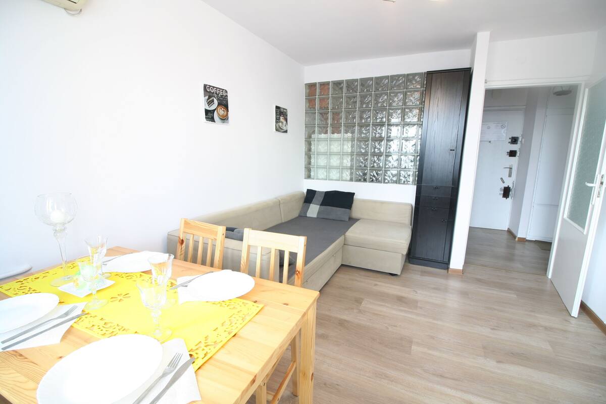 A compact living space with a dining area, a sofa bed, and a kitchen area.