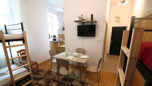 A compact living space with a bunk bed, a dining area with a table and chairs, a mounted TV, and a kitchen in the background. - Apartamenty Varsovie Chmielna (Warsaw)