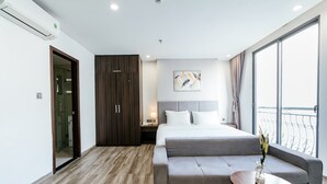 A modern hotel room with a bed, grey sofa, wooden floor, and a large window with a balcony.
