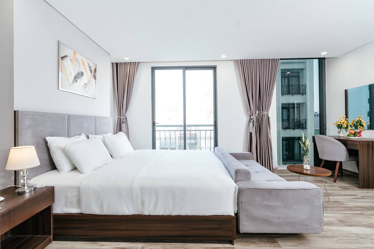 A modern hotel room with a large bed, a sofa, a desk, and a balcony view.