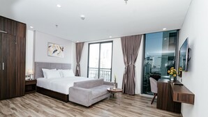 A modern hotel room with a large bed, a desk, and a view of the city through a large window.