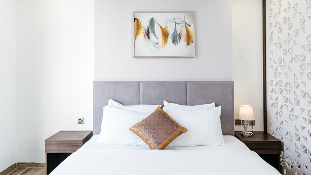 A hotel room with a bed, a nightstand, a wall-mounted lamp, and a decorative wall panel.