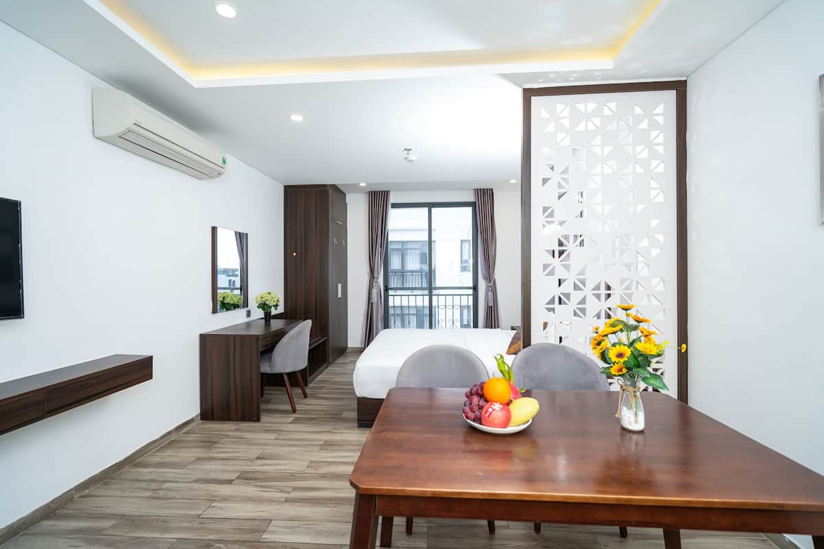 A hotel room with a wooden dining table, a fruit bowl, and a vase of flowers.