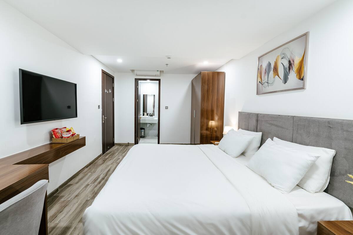 A modern hotel room with a large bed, a flat-screen TV, a wooden nightstand, and a painting on the wall.