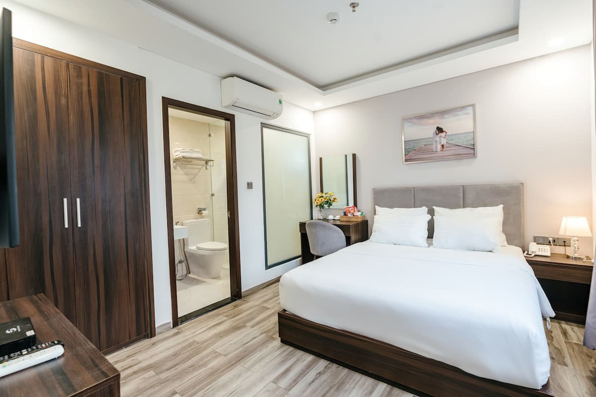 A modern hotel room with a large bed, a wardrobe, a bathroom with a glass door, and a painting on the wall.