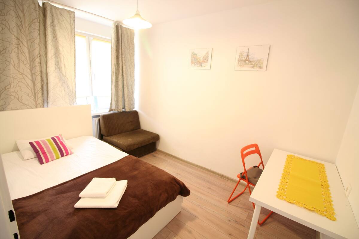 A bedroom with a bed, a sofa, a table, and two framed pictures on the wall.