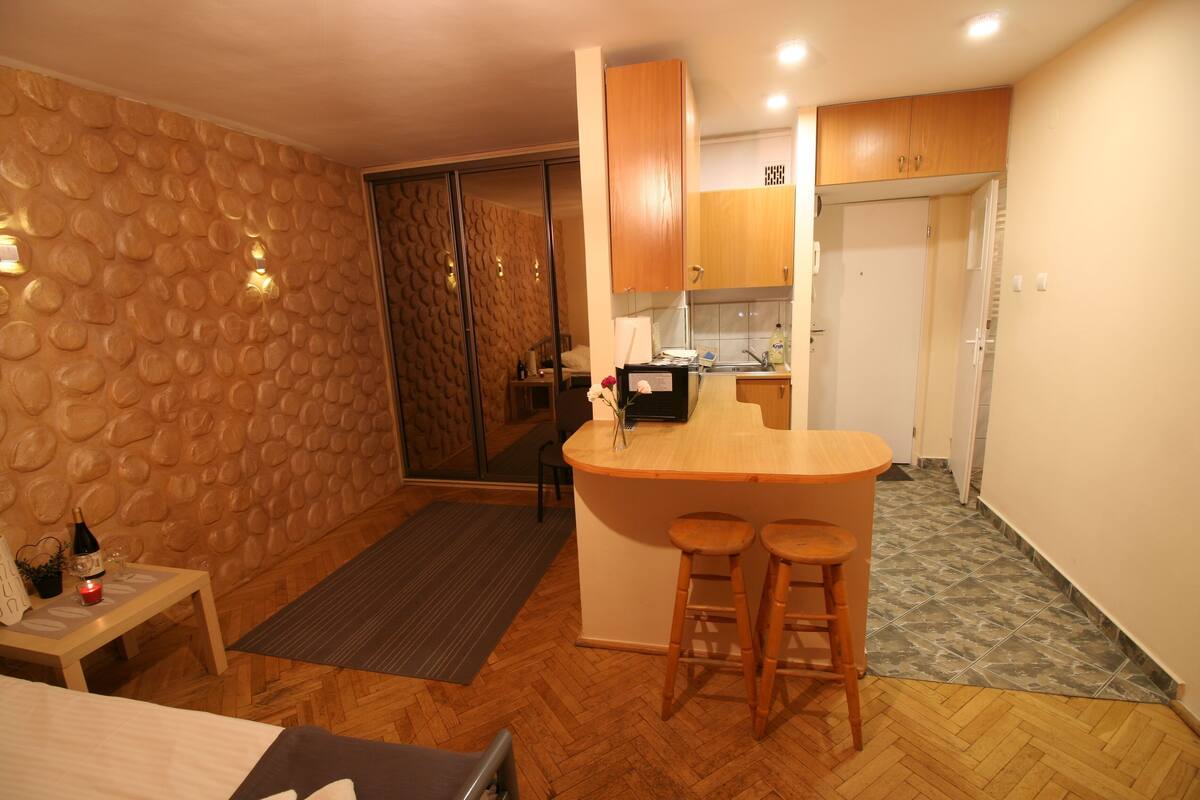 A compact kitchen with wooden cabinets, a small bar area, and a dining table with stools.
