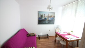 Ett rum med trägolv, en lila soffa, ett matbord med stolar och en målning som föreställer en kanalvy.