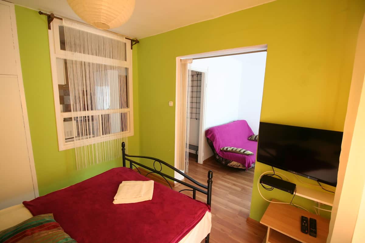 A bedroom with a bed, a TV, and a window with curtains.