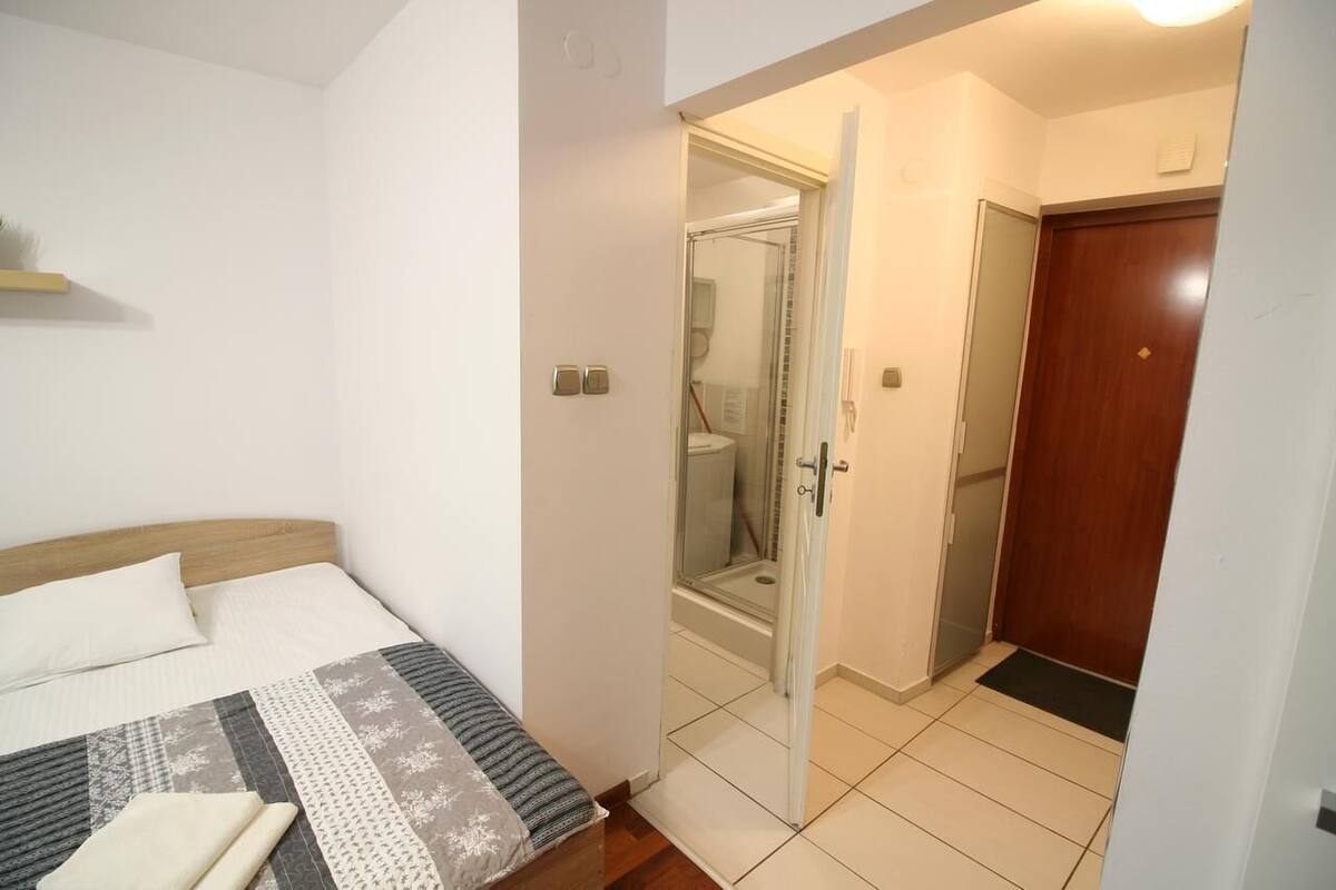 A bedroom with a bed, a bedside table, a nightstand, a door leading to a bathroom, and a wooden door.