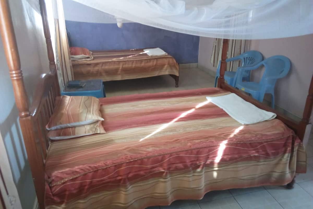 A room with two single beds, a wooden headboard, a mosquito net, and a blue plastic chair.