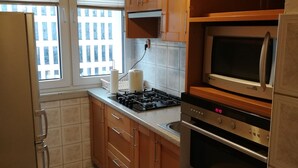 A kitchen with wooden cabinets, a microwave, an oven, a gas stove, and two stools. - Apartamenty Varsovie Jerozolimskie City (Warsaw)