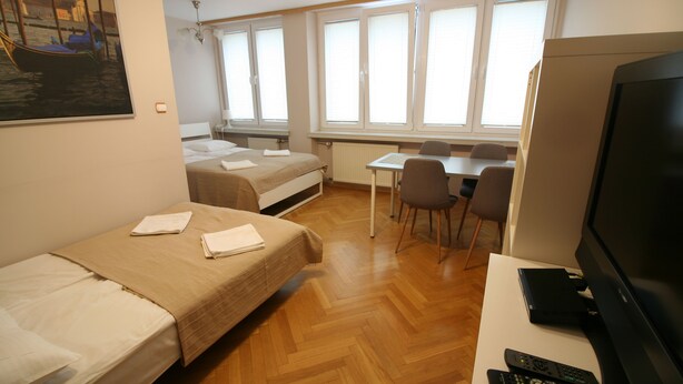 A hotel room with two single beds, a desk with a chair, a television, and a window with blinds. - Apartamenty Varsovie Jerozolimskie City (Warsaw)