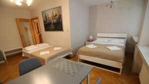 A room with two beds, a table, and a chair. There is a painting on the wall and a door with a mirror. - Apartamenty Varsovie Jerozolimskie City (Warsaw)