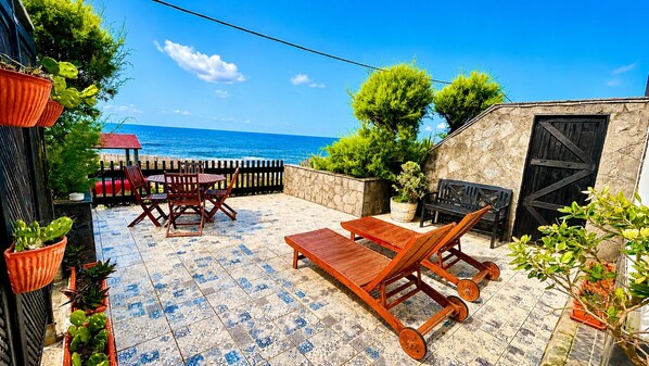 A patio with a view of the sea, wooden furniture, and potted plants. - Sea Roots "Sea zone" - Amazing sunsets and ocean views (Mosteiros)