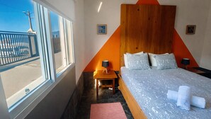 Une chambre d’hôtel avec un grand lit, une tête de lit en bois, une table de chevet, une fenêtre donnant sur la rue et un tapis rouge.