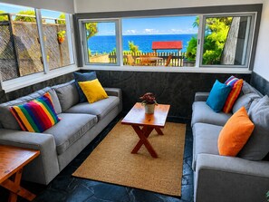 A room with two grey sofas, a wooden coffee table, and a view of the ocean through large windows. - Sea Roots "Sea zone" - Amazing sunsets and ocean views (Mosteiros)