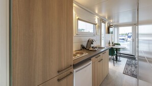 A modern kitchen with wooden cabinets, a built-in stove, and a dining area with a table and chairs. - Cozy floating Boatlodge "Mallorca", Max. 4 pers, 2 bedrooms. (Maastricht)