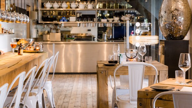 A restaurant interior with a wooden bar, white chairs, and a variety of glassware and dishes on display. - Cozy floating Boatlodge "Mallorca", Max. 4 pers, 2 bedrooms. (Maastricht)