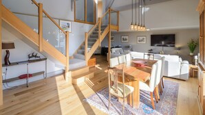 A spacious living area with a wooden staircase, a dining table, and a sofa set.