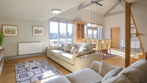 A spacious living room with a sofa, a dining table, and a staircase.