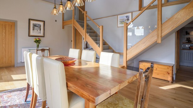A dining area with a wooden table, white chairs, and a staircase.