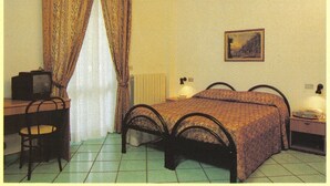 A bedroom with a bed, a desk, a chair, a nightstand, a lamp, and a painting on the wall. - Hotel San Francesco Inn (Stroncone)