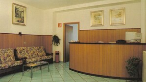A reception area with a wooden reception desk, two patterned sofas, a small table, and a potted plant. - Hotel San Francesco Inn (Stroncone)