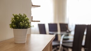Una planta en maceta sobre una mesa de madera, en una habitación con una mesa de comedor y sillas al fondo.