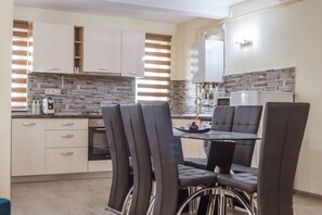 A modern kitchen with a dining area, featuring a table with chairs, a built-in oven, and a refrigerator. - Dany Luxury Apartment (Pitesti)