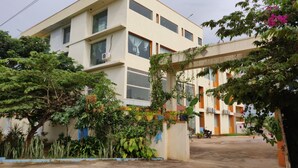A multi-story building with a flat roof, surrounded by lush greenery and trees.