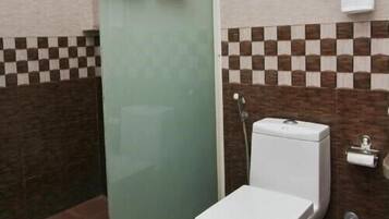 Un baño con inodoro, mampara de vidrio y toallero.