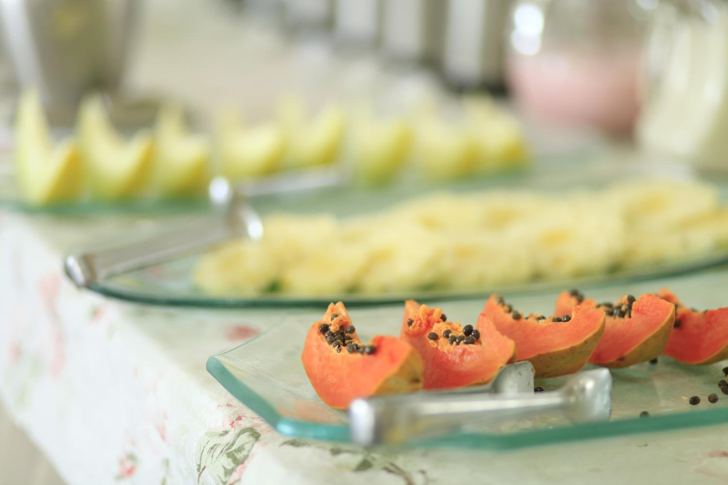 A glass serving tray with sliced papaya and pineapple on a floral tablecloth.