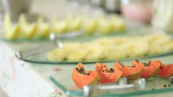 A glass serving tray with sliced papaya and pineapple on a floral tablecloth.