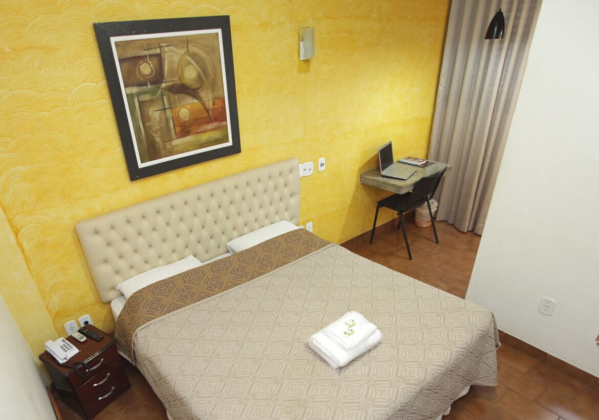 Habitación de hotel con cama, escritorio, silla, un cuadro en la pared y teléfono en la mesita de noche.
