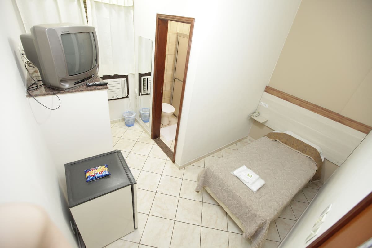 Habitación de hotel pequeña con cama, televisor, una mesita y baño visible a través de una puerta abierta.