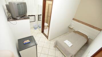 Ein kleines Hotelzimmer mit Bett, Fernseher, einem kleinen Tisch und einem durchgegangene Tür erkennbaren Badezimmer.