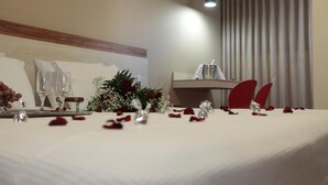 A hotel room with a neatly made bed, a bedside table with a glass and a vase, and a window with curtains. - Hotel Pouso Novo (Matao)