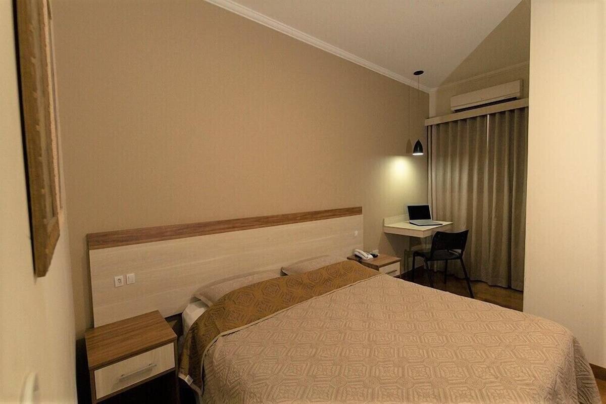 Habitación de hotel con una cama, un escritorio con una computadora portátil, una silla y un equipo de aire acondicionado.