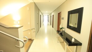 A hotel hallway with a handrail, a mirror, and a plant on a console table. - Hotel Pouso Novo (Matao)