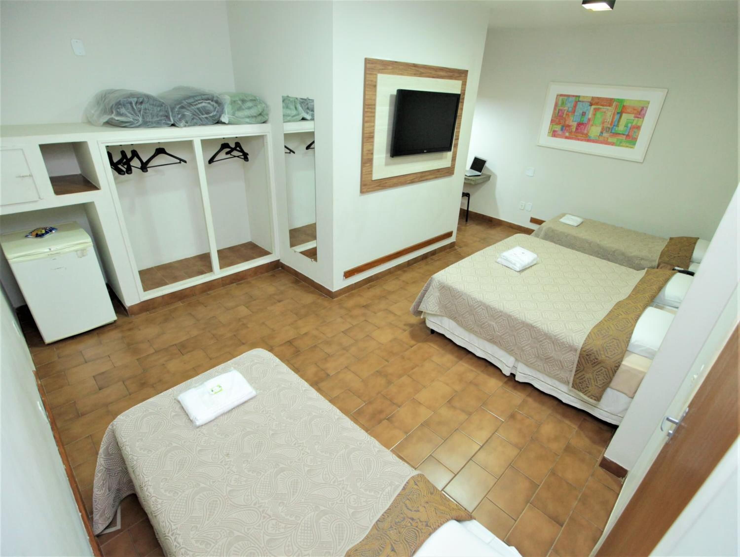 A hotel room with two beds, a TV mounted on the wall, a small desk with a chair, and a wardrobe with hangers.
