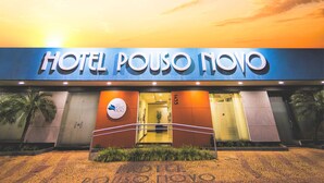 The exterior of Hotel Pouso Novo with a clear entrance, a palm tree, and a sunset in the background. - Hotel Pouso Novo (Matao)