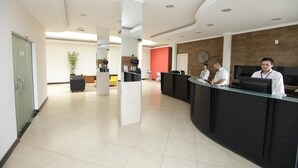 A reception area with a black reception desk, a plant, and a red accent wall. - Hotel Pouso Novo (Matao)
