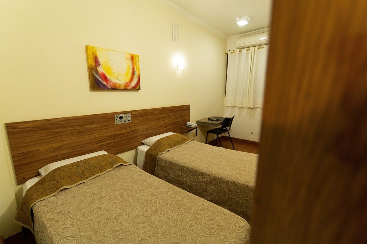 Habitación de hotel con dos camas, un escritorio, una silla y un cuadro en la pared.