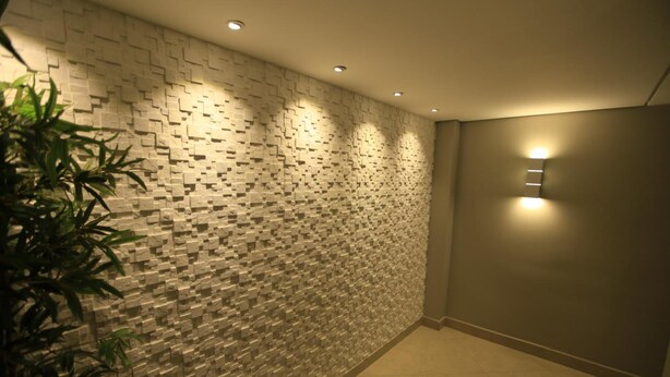 A modern interior with a textured wall, recessed ceiling lights, and a potted plant. - Hotel Pouso Novo (Matao)